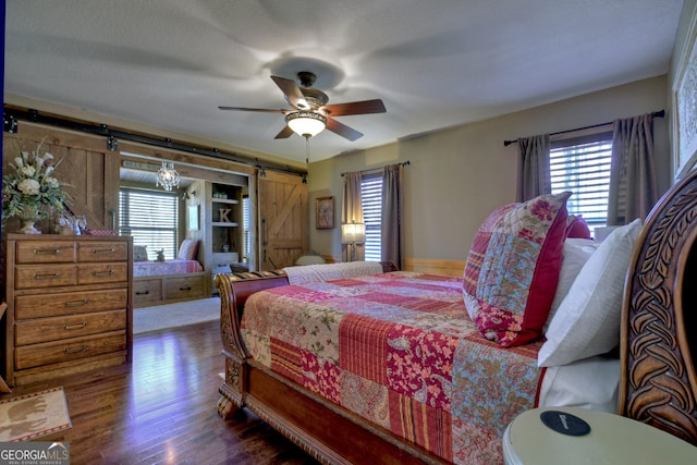 bedroom with a ceiling fan, wood finished floors, and a barn door