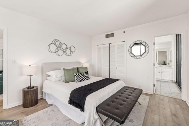 bedroom featuring baseboards, visible vents, ensuite bath, light wood-type flooring, and a closet