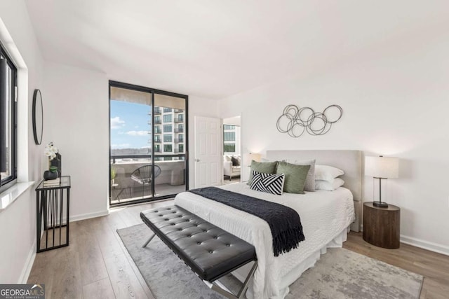 bedroom featuring access to outside, floor to ceiling windows, wood finished floors, and baseboards