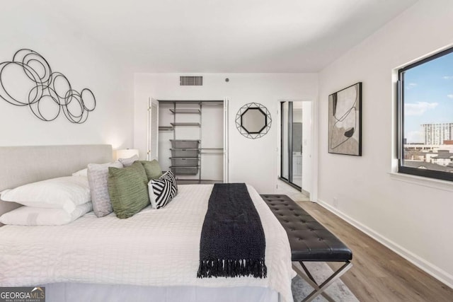 bedroom with a closet, wood finished floors, visible vents, and baseboards