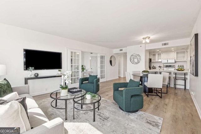 living room with french doors, visible vents, baseboards, and light wood finished floors