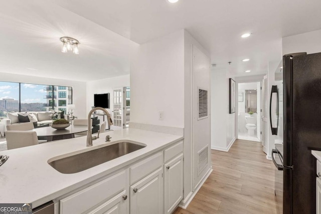 kitchen featuring freestanding refrigerator, light countertops, light wood-style floors, white cabinetry, and a sink