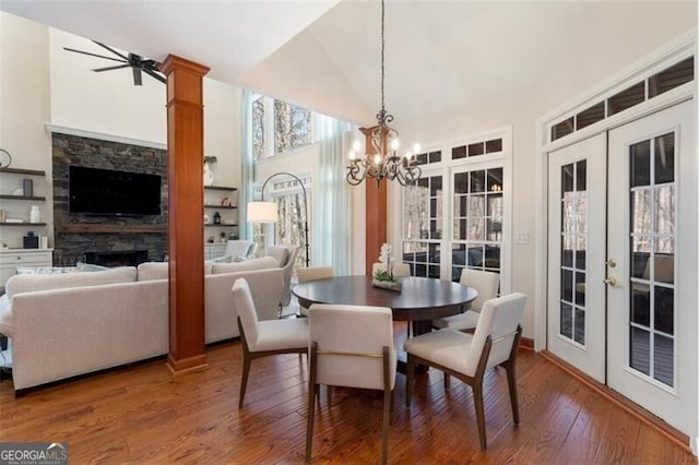 dining area featuring french doors, high vaulted ceiling, a stone fireplace, a chandelier, and hardwood / wood-style flooring