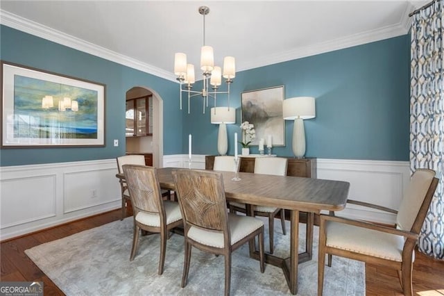 dining area featuring arched walkways, a wainscoted wall, wood finished floors, an inviting chandelier, and crown molding