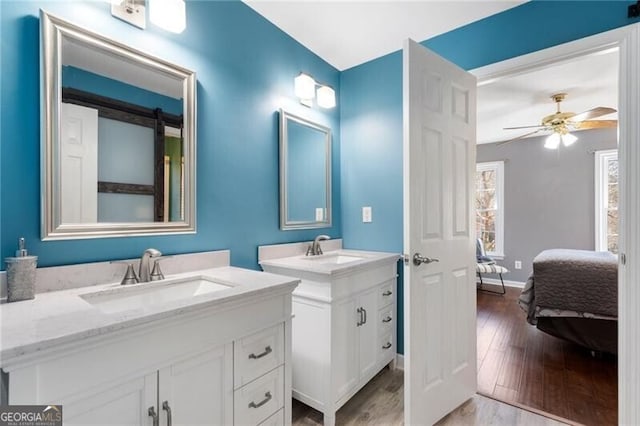 bathroom featuring wood finished floors, two vanities, a sink, and connected bathroom