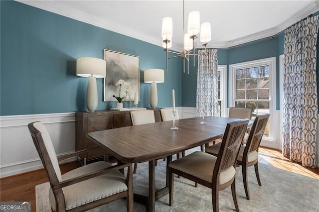 dining space featuring ornamental molding, wood finished floors, a wainscoted wall, and an inviting chandelier