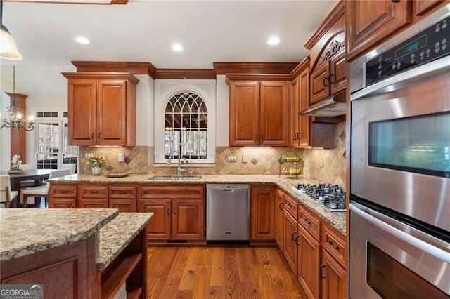 kitchen featuring appliances with stainless steel finishes, light stone counters, wood finished floors, hanging light fixtures, and a sink