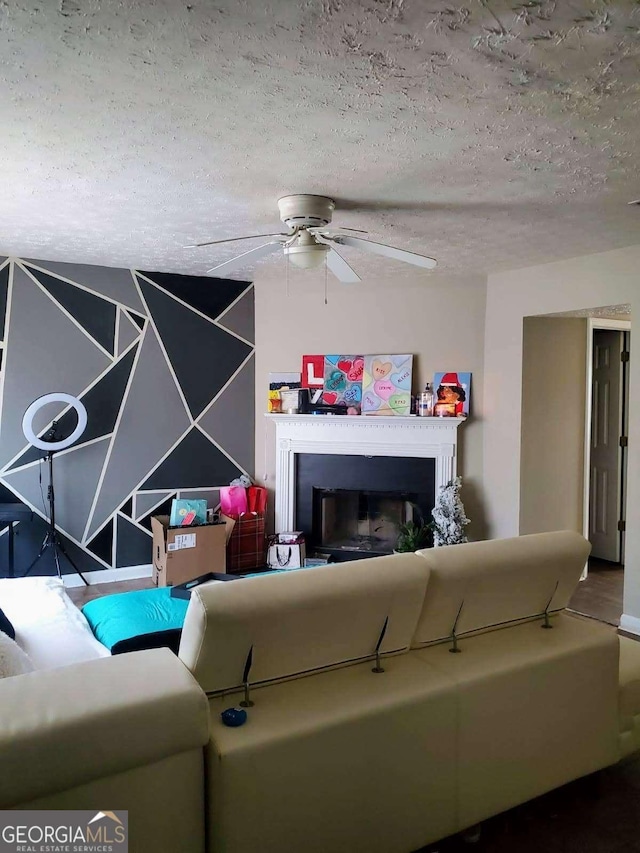 living area featuring a fireplace, a ceiling fan, and a textured ceiling