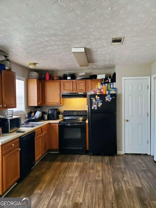 kitchen with under cabinet range hood, visible vents, light countertops, dark wood-style floors, and black appliances