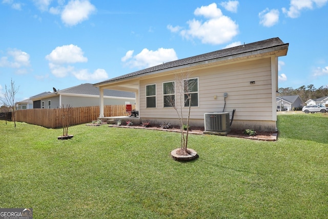 rear view of property featuring central air condition unit, fence, and a yard