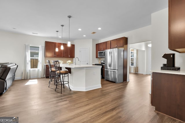 kitchen featuring a breakfast bar area, light countertops, appliances with stainless steel finishes, open floor plan, and wood finished floors