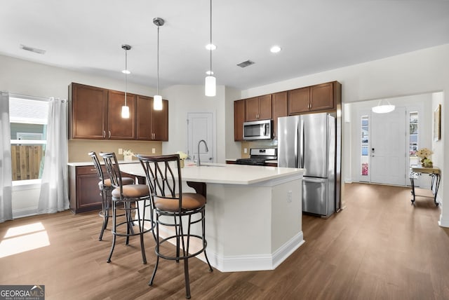 kitchen with stainless steel appliances, light countertops, visible vents, a sink, and wood finished floors