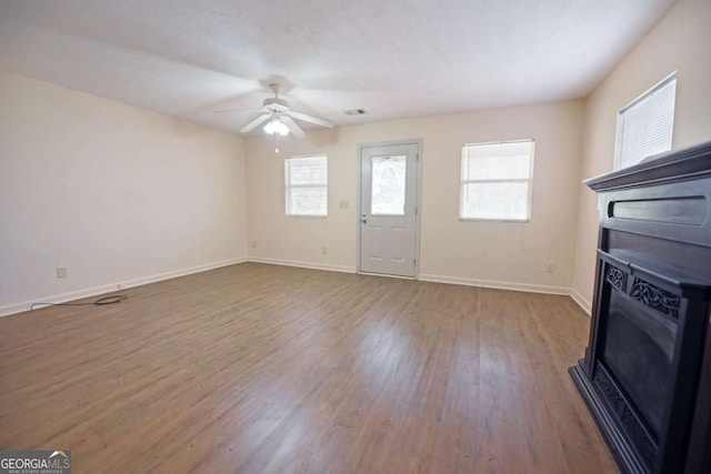 unfurnished living room with ceiling fan, baseboards, and wood finished floors