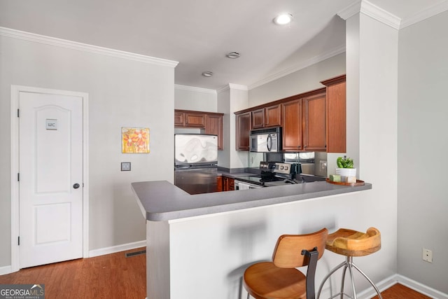 kitchen with appliances with stainless steel finishes, crown molding, a kitchen breakfast bar, and wood finished floors