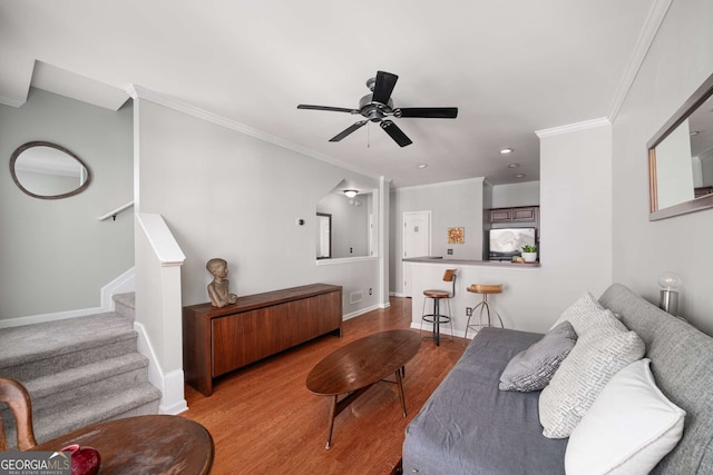 living area featuring wood finished floors, a ceiling fan, baseboards, ornamental molding, and stairway