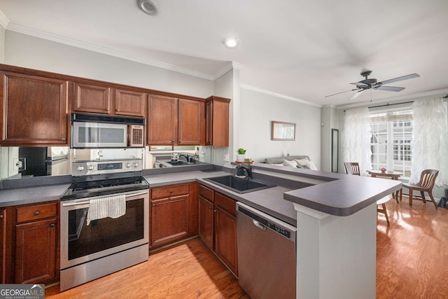 kitchen with appliances with stainless steel finishes, ornamental molding, a peninsula, light wood-style floors, and a sink