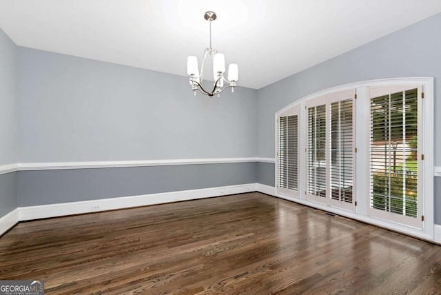 spare room featuring a notable chandelier, baseboards, and wood finished floors