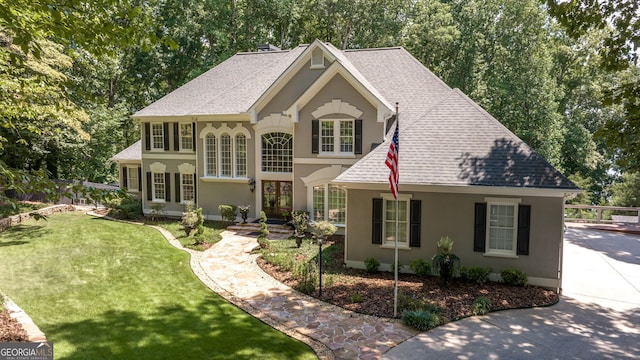 view of front facade with stucco siding, a shingled roof, and a front lawn