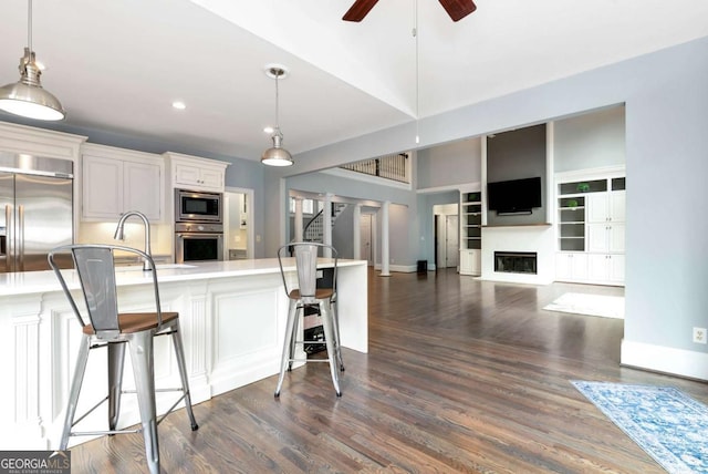 kitchen featuring dark wood-type flooring, a breakfast bar, a ceiling fan, light countertops, and built in appliances