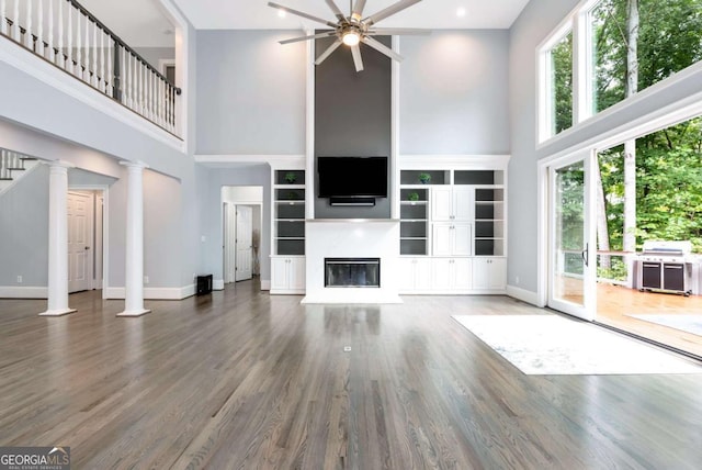 unfurnished living room with baseboards, a high ceiling, wood finished floors, a glass covered fireplace, and a ceiling fan