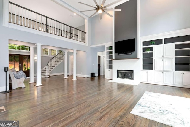 unfurnished living room featuring baseboards, ceiling fan, a fireplace with flush hearth, decorative columns, and wood finished floors