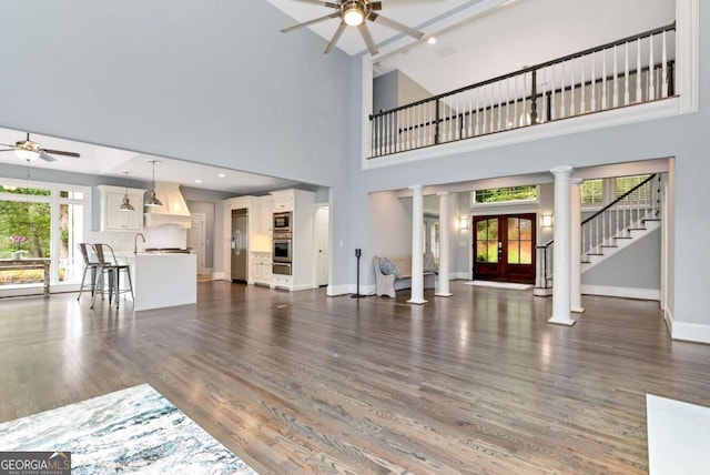 unfurnished living room featuring dark wood-style floors, a high ceiling, ceiling fan, decorative columns, and baseboards