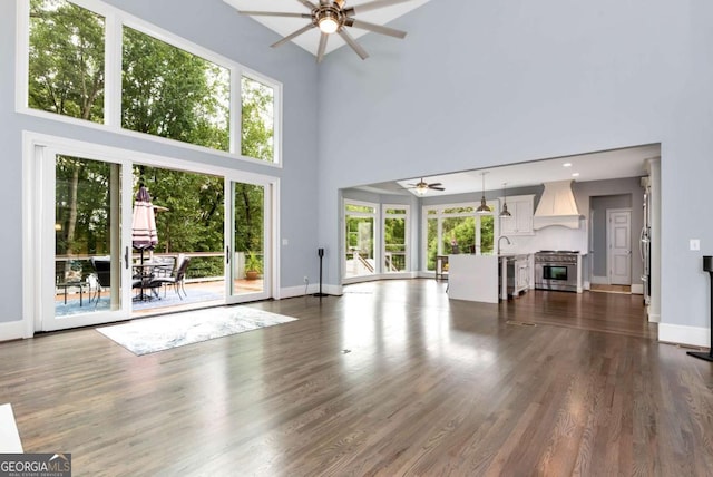 unfurnished living room featuring dark wood-style flooring, a sink, baseboards, a ceiling fan, and a high ceiling