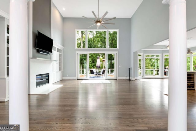 unfurnished living room featuring a high ceiling, ceiling fan, decorative columns, and beverage cooler