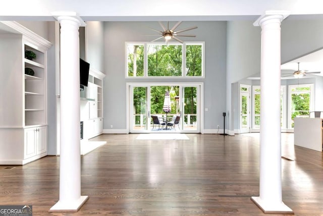 unfurnished living room with a towering ceiling, a ceiling fan, dark wood-style flooring, and ornate columns