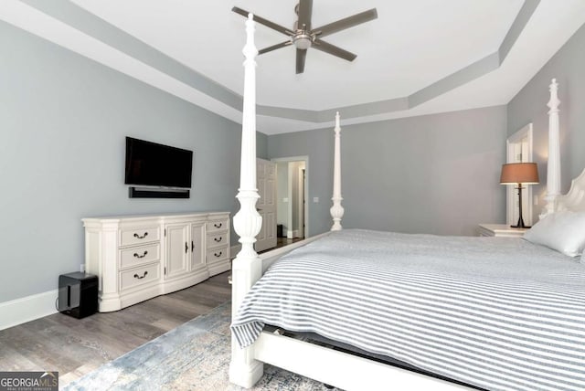 bedroom featuring wood finished floors, ceiling fan, a tray ceiling, and baseboards