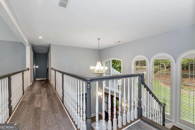 hall featuring wood finished floors, a chandelier, attic access, baseboards, and visible vents