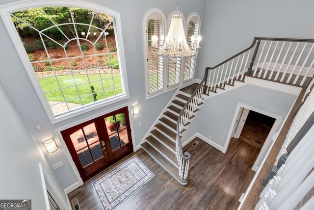 foyer entrance featuring an inviting chandelier, stairway, baseboards, a towering ceiling, and french doors
