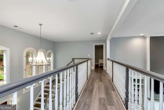 hallway featuring visible vents, wood finished floors, a healthy amount of sunlight, and a chandelier