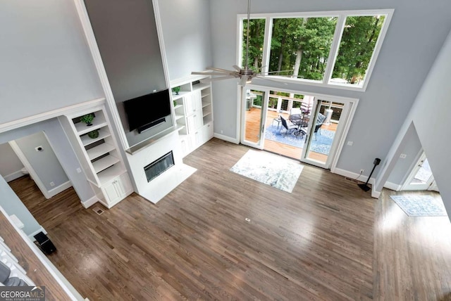 unfurnished living room with baseboards, wood finished floors, a fireplace with flush hearth, and a towering ceiling