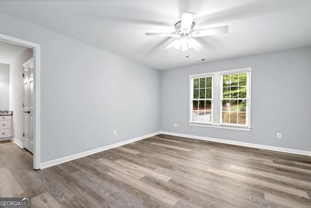spare room with wood finished floors, a ceiling fan, and baseboards