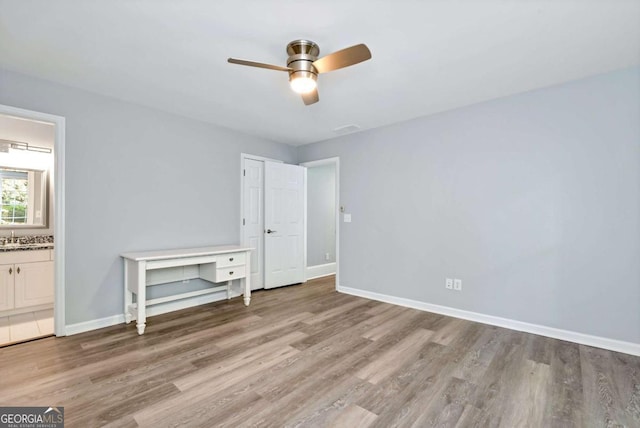 unfurnished bedroom featuring baseboards, ceiling fan, ensuite bathroom, and light wood finished floors