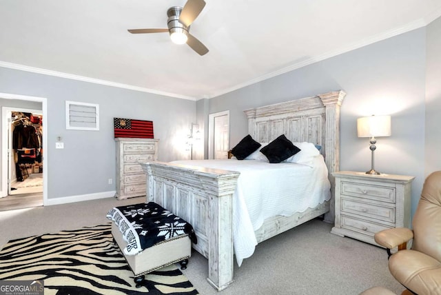 bedroom with a walk in closet, ornamental molding, a ceiling fan, carpet flooring, and baseboards