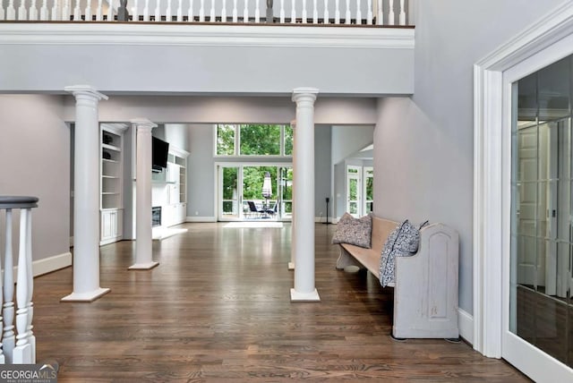 interior space with a fireplace, dark wood-style floors, decorative columns, and baseboards