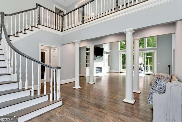interior space with a high ceiling, stairs, baseboards, ornate columns, and wood finished floors
