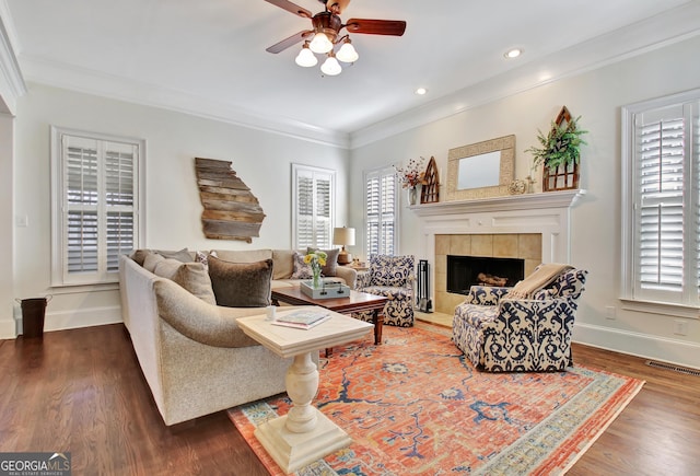 living room with baseboards, visible vents, a tiled fireplace, ornamental molding, and wood finished floors