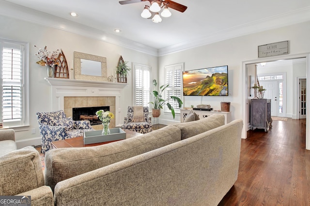 living area with dark wood-type flooring, a ceiling fan, baseboards, ornamental molding, and a tiled fireplace