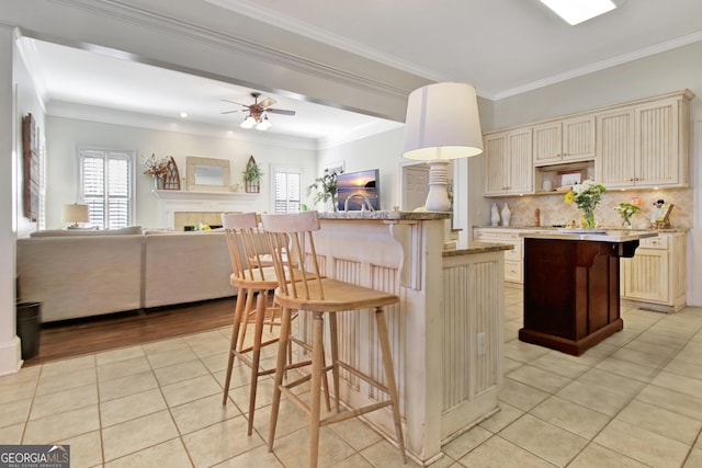 kitchen with a center island with sink, a kitchen breakfast bar, cream cabinetry, and light tile patterned flooring