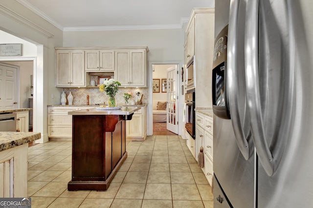 kitchen with light tile patterned floors, stainless steel appliances, tasteful backsplash, cream cabinets, and ornamental molding