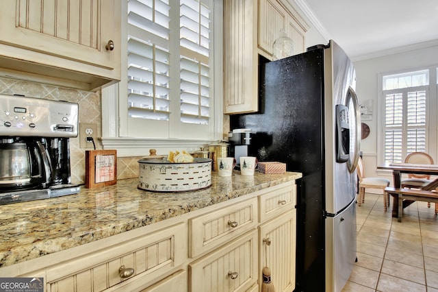 kitchen with cream cabinetry, crown molding, stainless steel refrigerator with ice dispenser, decorative backsplash, and light tile patterned flooring