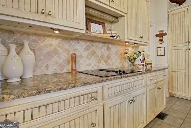 kitchen featuring decorative backsplash, black electric stovetop, cream cabinets, and light tile patterned floors