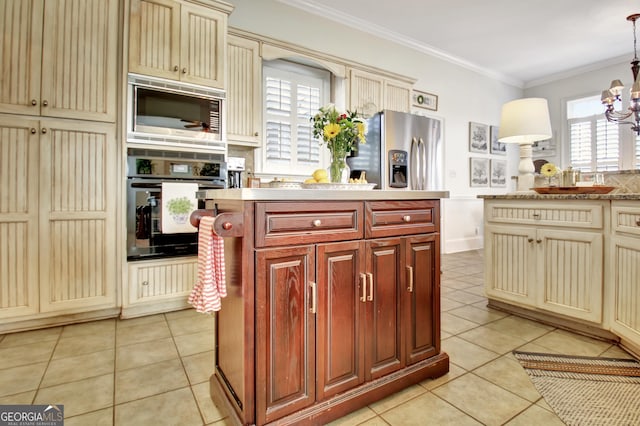 kitchen with light tile patterned flooring, a notable chandelier, cream cabinetry, appliances with stainless steel finishes, and crown molding