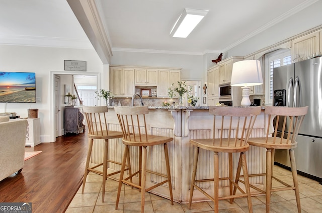 kitchen featuring light wood finished floors, decorative backsplash, ornamental molding, stainless steel appliances, and cream cabinetry