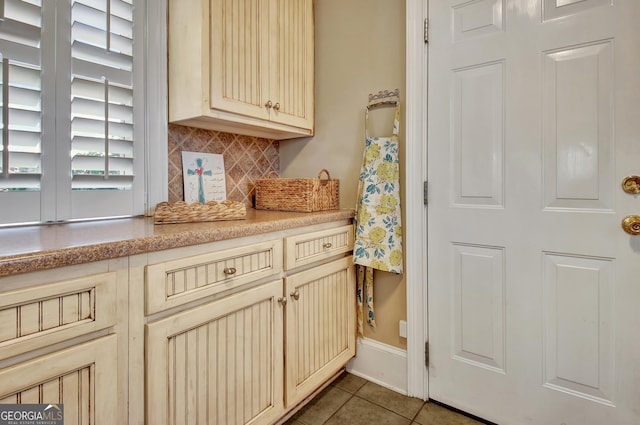 kitchen featuring tile patterned floors, baseboards, light countertops, cream cabinetry, and decorative backsplash