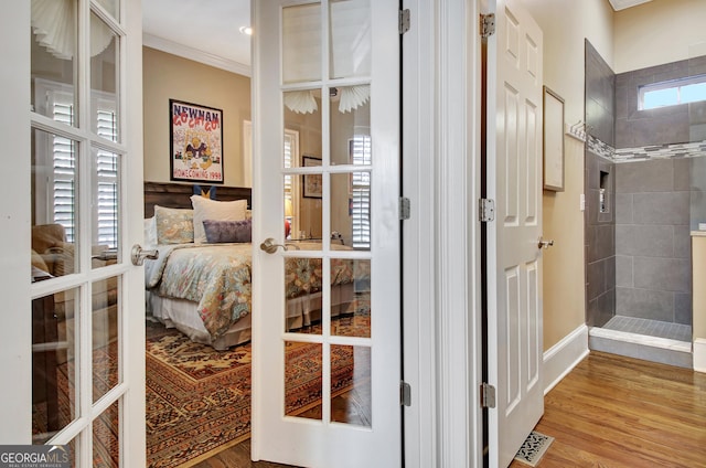 interior space with wood finished floors, french doors, ensuite bath, and ornamental molding