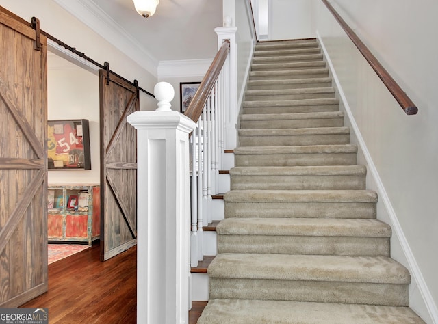 staircase with wood finished floors, crown molding, and a barn door